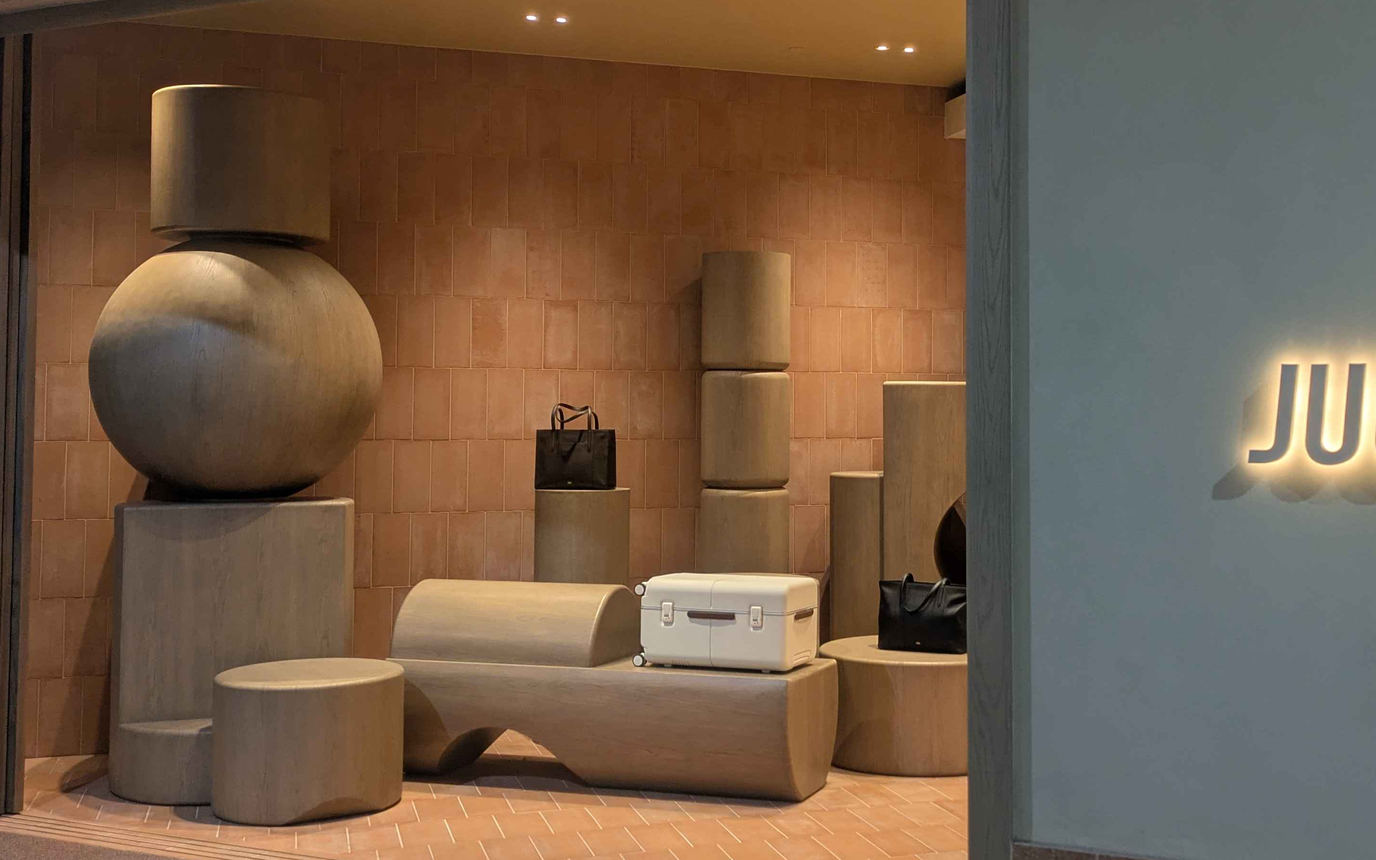 Solitary white carry-on suitcase displayed beside wooden sculptures in July showroom window